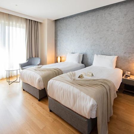 Dosso Dossi Hotels & Spa Downtown Istanbul Exterior photo The photo shows a modern hotel room featuring two single beds with white linens and soft gray throw blankets. The room has a stylish design, with wooden flooring and a large window dressed with light curtains that allow natural light to enter. There'