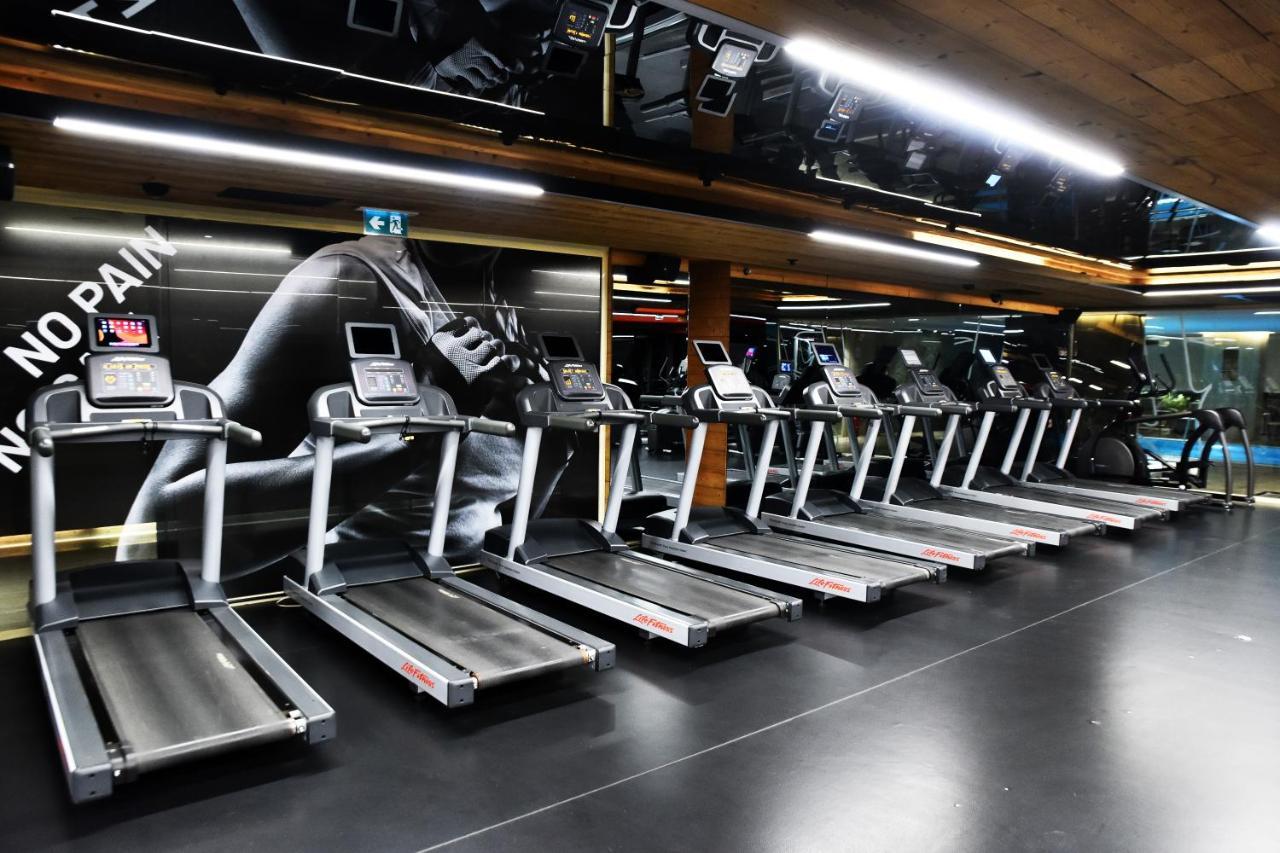Dosso Dossi Hotels & Spa Downtown Istanbul Exterior photo The photo shows a row of treadmills in a gym setting. The treadmills are modern and aligned next to each other on a sleek black floor. The background features a large image of a runner's foot, with motivational phrases that suggest themes of fitness 
