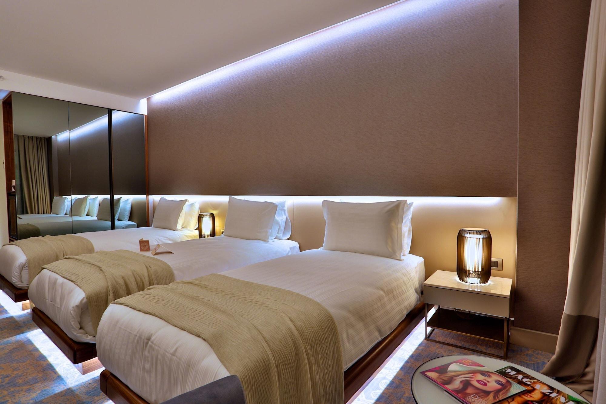 Dosso Dossi Hotels & Spa Downtown Istanbul Exterior photo The photo shows a modern hotel room with two neatly made beds. Each bed is dressed with white linens and has a light-colored throw blanket. There are stylish bedside lamps on either side of the beds, as well as small nightstands. The wall behind the 