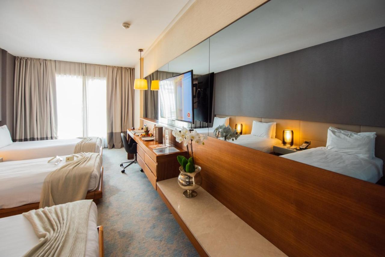 Dosso Dossi Hotels & Spa Downtown Istanbul Exterior photo The photo shows a modern hotel room featuring two beds with light-colored bedding. There is a large mirror above a wooden dresser, which holds some decorative items, including a small plant. A TV is mounted on the wall, and there is a workspace with 