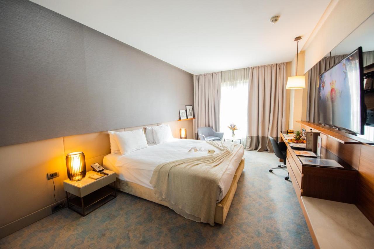 Dosso Dossi Hotels & Spa Downtown Istanbul Exterior photo The photo shows a modern hotel room with a comfortable layout. There's a large bed with white linens and a soft throw blanket. Beside the bed, there are bedside tables with lamps. A window covered with sheer curtains allows natural light to enter the