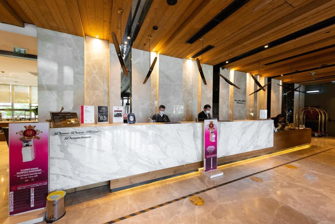 Dosso Dossi Hotels & Spa Downtown Istanbul Exterior photo The photo shows a hotel reception area. The front desk is made of elegant marble, and the space features wooden accents on the ceiling. Behind the counter, two staff members are visible, likely assisting guests. There are signs and promotional materi
