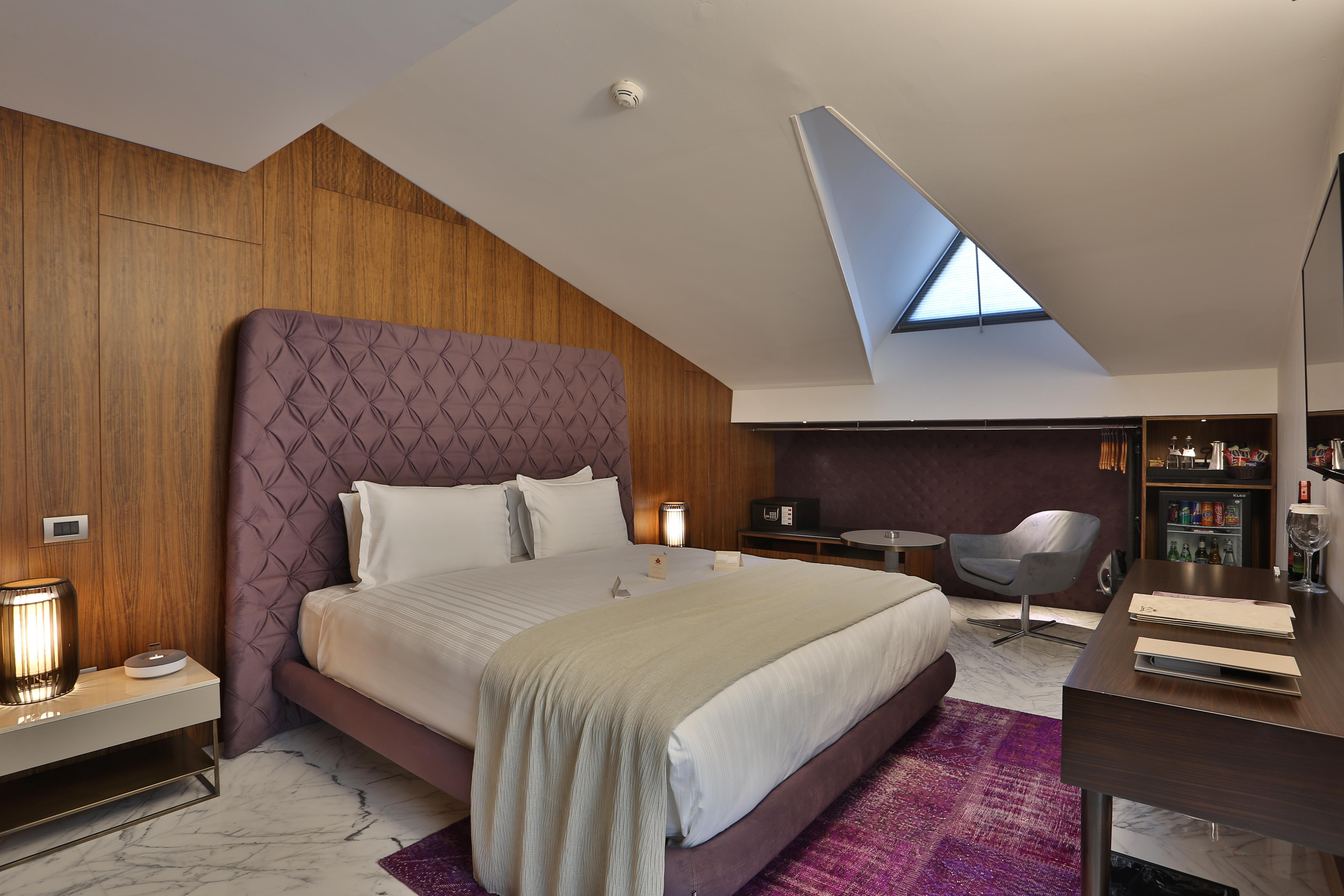 Dosso Dossi Hotels & Spa Downtown Istanbul Exterior photo The photo shows a stylish hotel room with a modern design. It features a large bed with a tufted purple headboard, complemented by white bedding and a light gray throw. The walls are made of wooden panels, adding warmth to the space. To the side, the