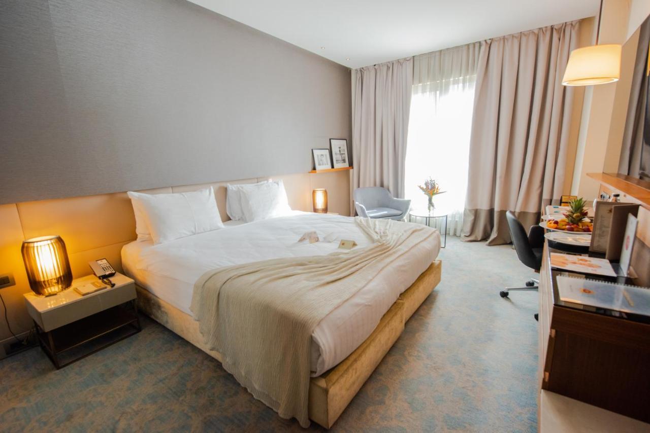 Dosso Dossi Hotels & Spa Downtown Istanbul Exterior photo The photo showcases a modern hotel room featuring a king-sized bed with white bedding and a light-colored throw. There are elegant bedside lamps on either side of the bed and a small nightstand. A large window dressed with soft, light-colored curtain