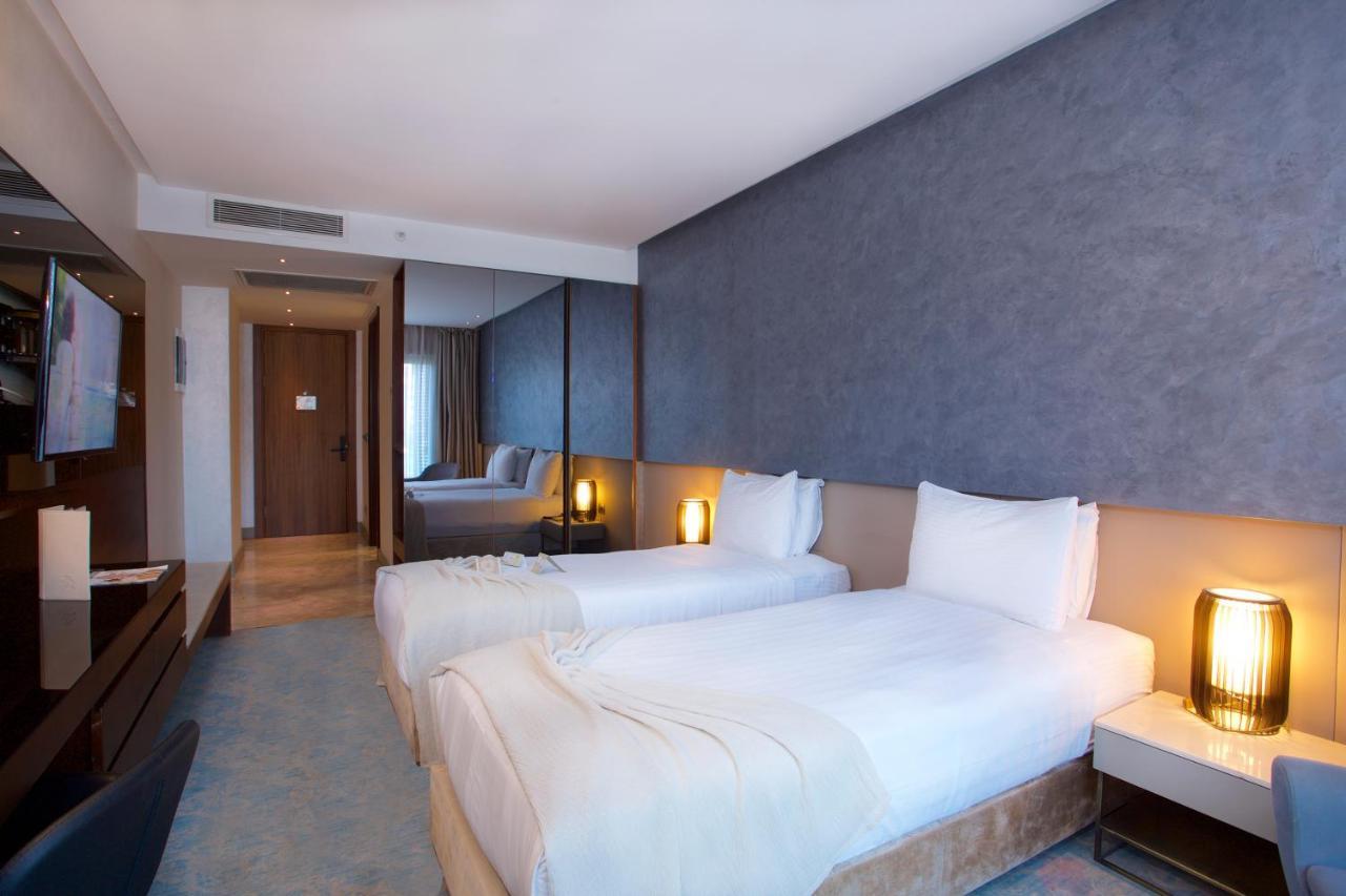 Dosso Dossi Hotels & Spa Downtown Istanbul Exterior photo The photo shows a modern hotel room featuring two single beds with white bedding. The walls have a stylish gray finish, and there is a decorative element behind the beds. On either side of the beds, there are bedside tables with lamps. A flat-screen 