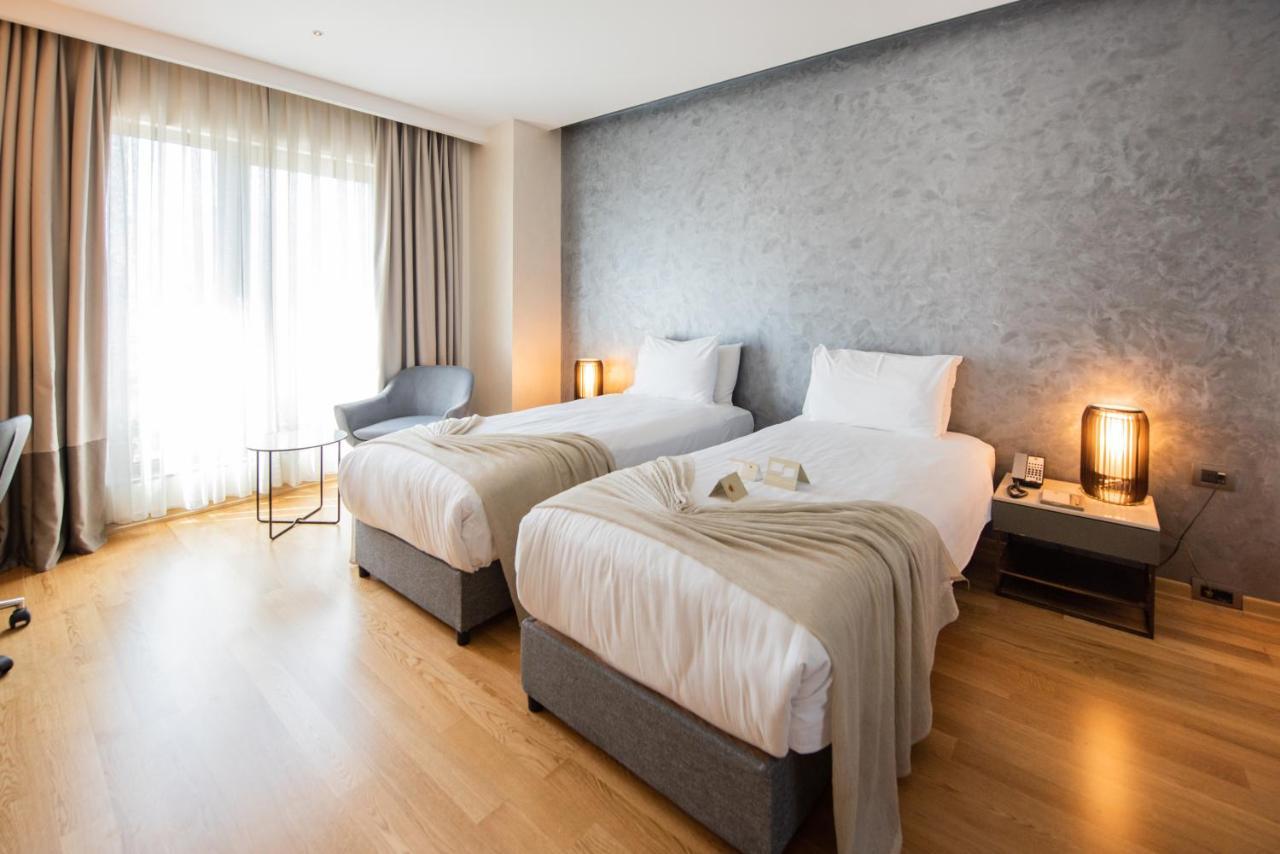 Dosso Dossi Hotels & Spa Downtown Istanbul Exterior photo The photo shows a modern hotel room featuring two single beds with white linens and soft gray throw blankets. The room has a stylish design, with wooden flooring and a large window dressed with light curtains that allow natural light to enter. There'