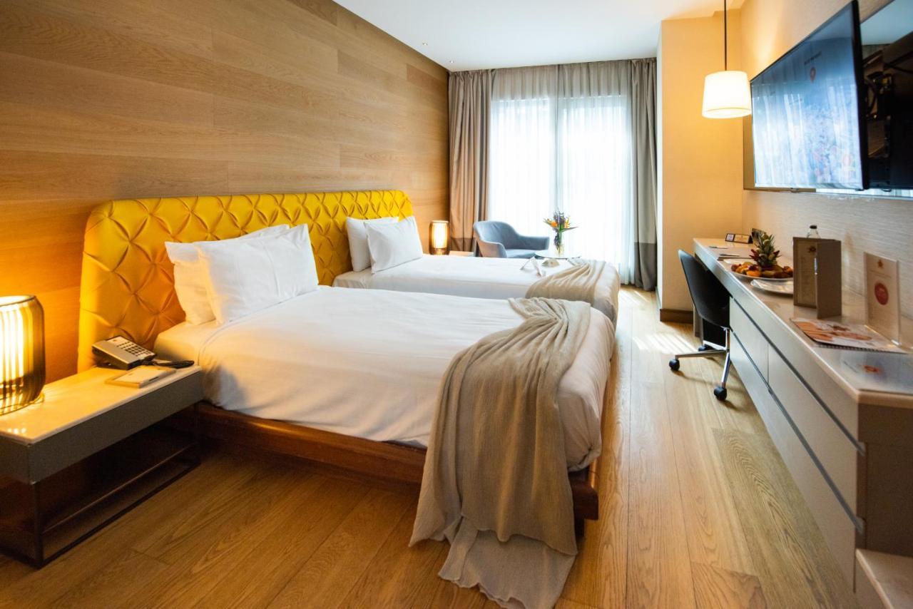 Dosso Dossi Hotels & Spa Downtown Istanbul Exterior photo The photo shows a stylish hotel room featuring two beds with white linens and a unique yellow headboard. The room has wooden walls and a polished wooden floor. There are large windows with sheer curtains allowing natural light to flood in. A small se