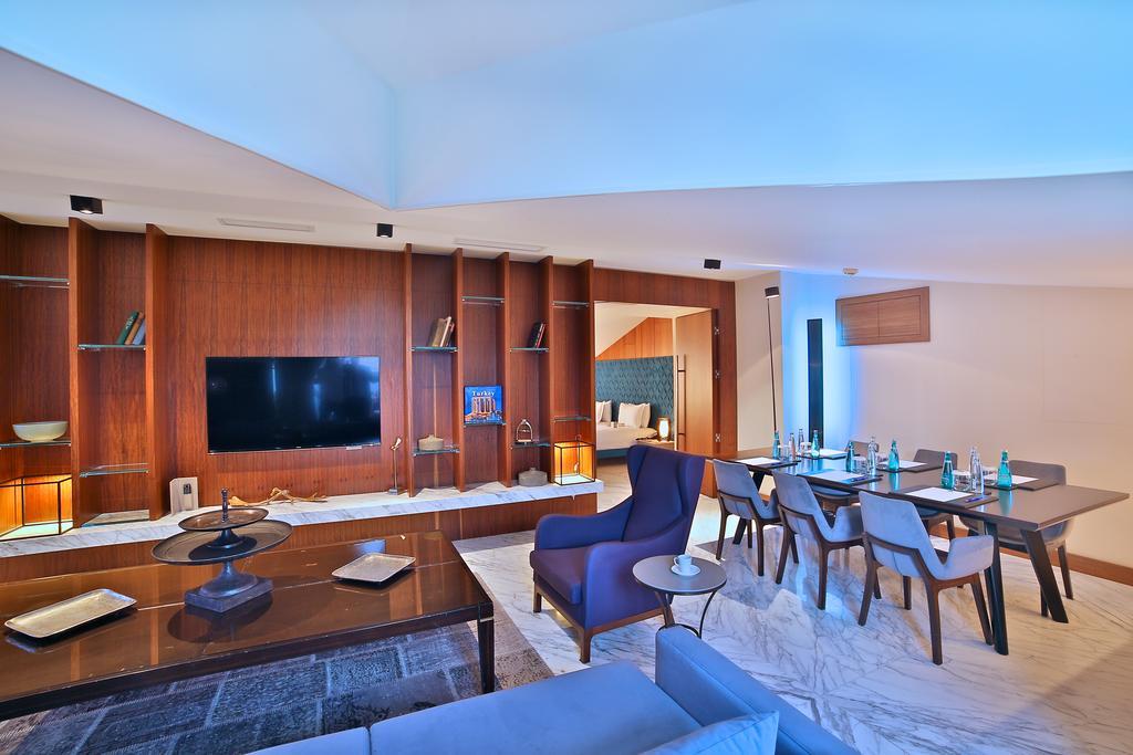 Dosso Dossi Hotels & Spa Downtown Istanbul Exterior photo The photo shows a modern living space that features an open layout. On the left, there is a comfortable seating area with a sofa and a coffee table. The wall opposite the seating area contains a large flat-screen TV mounted on a stylish wooden panel.