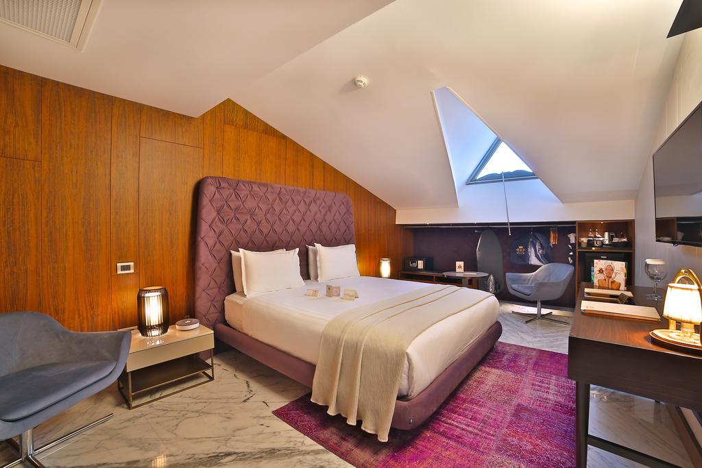 Dosso Dossi Hotels & Spa Downtown Istanbul Exterior photo The photo shows a modern hotel room featuring a stylish design. It has a large bed with a purple headboard, neatly made with white bedding. The walls are a warm wooden tone, and the room has slanted ceilings with a skylight that lets in natural light