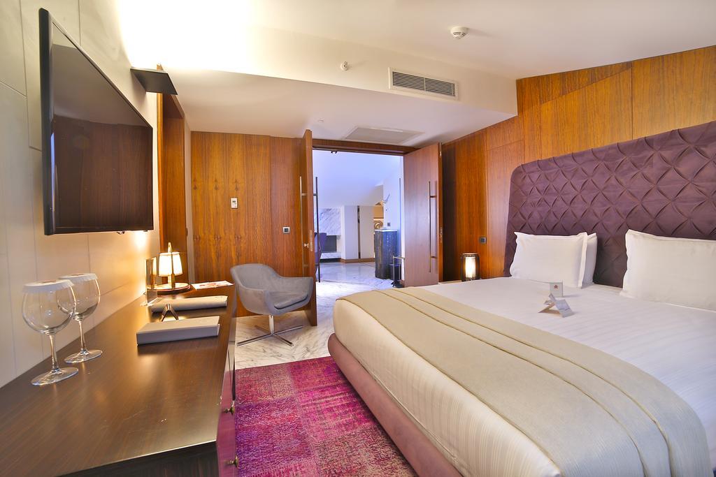 Dosso Dossi Hotels & Spa Downtown Istanbul Exterior photo The photo depicts a modern hotel room. It features a large bed with white linens and a decorative headboard in a rich purple hue. The room has wooden paneling on the walls, adding warmth to the space. There's a flat-screen TV mounted on the wall oppo